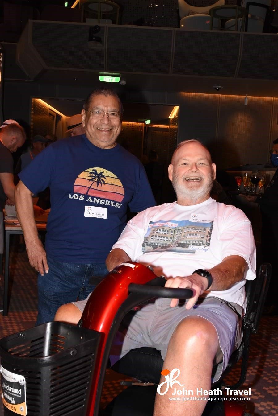 Two men are standing next to each other and one is sitting in a mobility scooter.