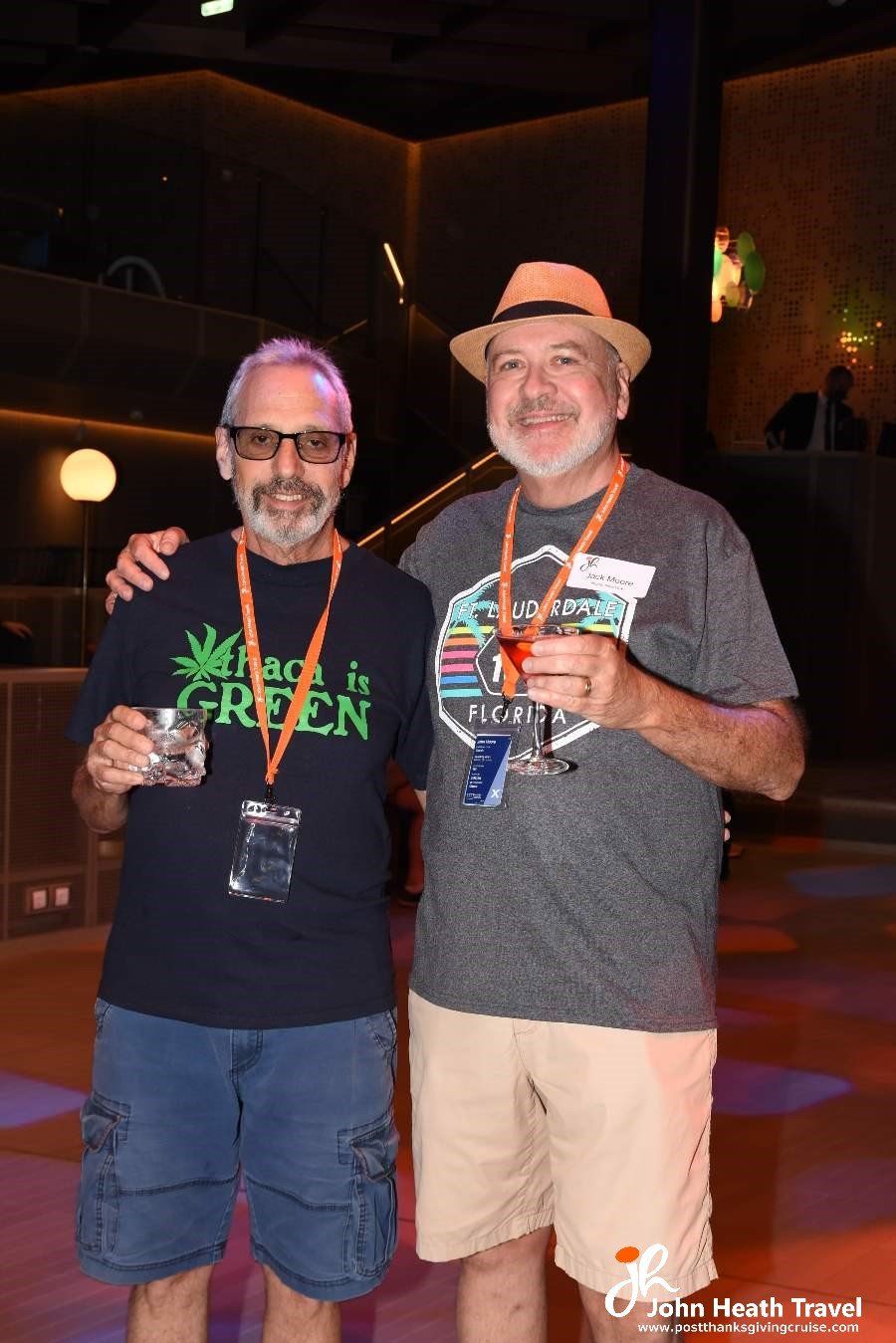 Two men are standing next to each other in a dark room holding drinks.