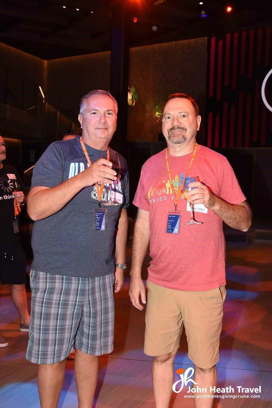 Two men are standing next to each other in a dark room holding drinks.