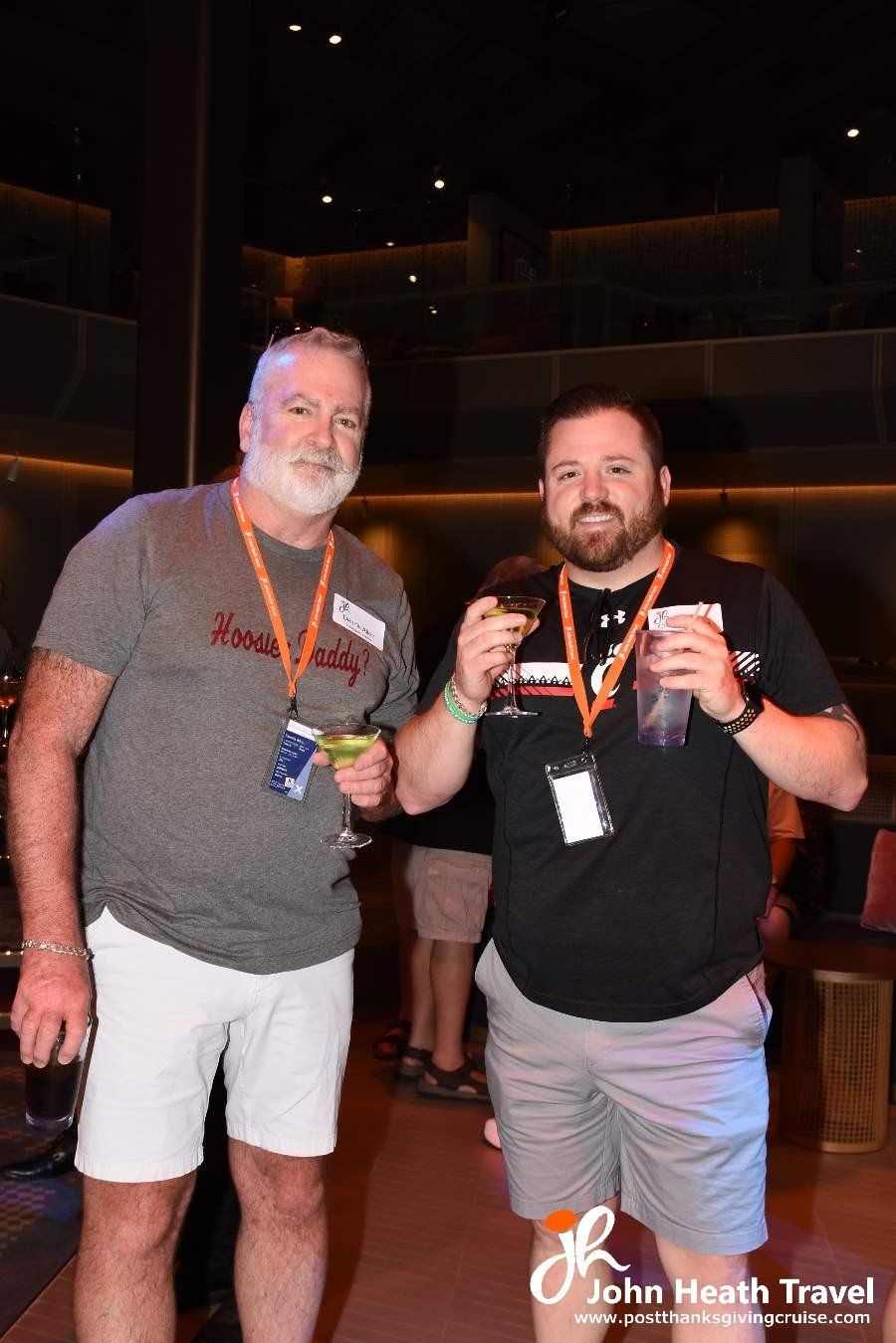Two men are standing next to each other in a dark room holding drinks.