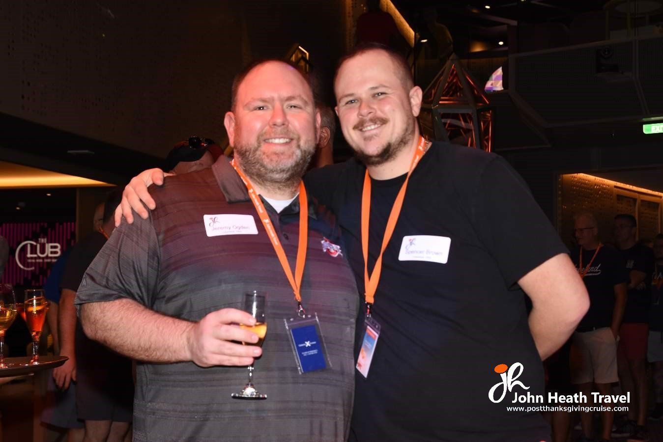 Two men are posing for a picture together and one of them is holding a glass of wine.