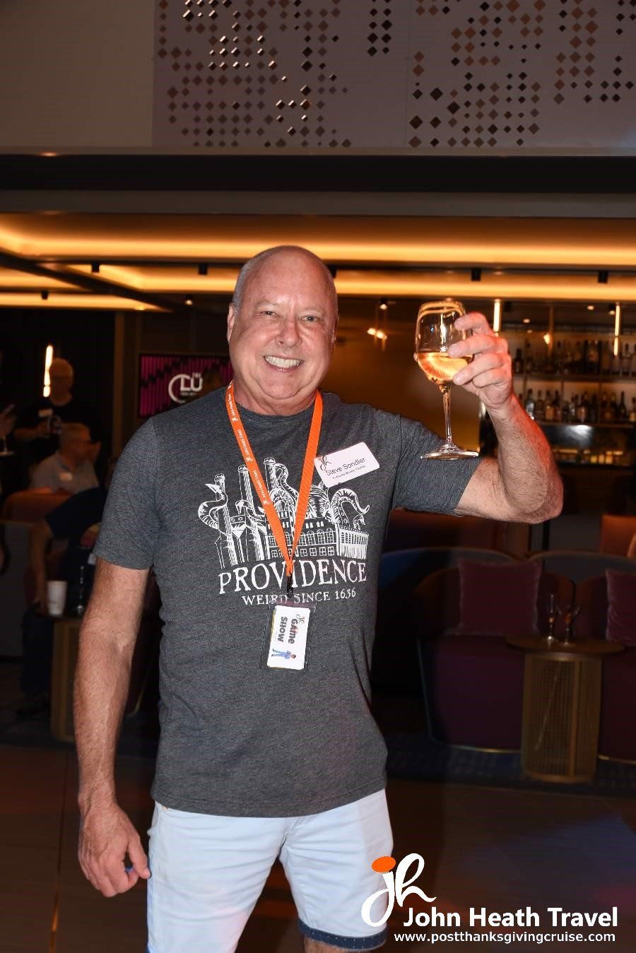 A man wearing a providence shirt is holding a glass of wine.