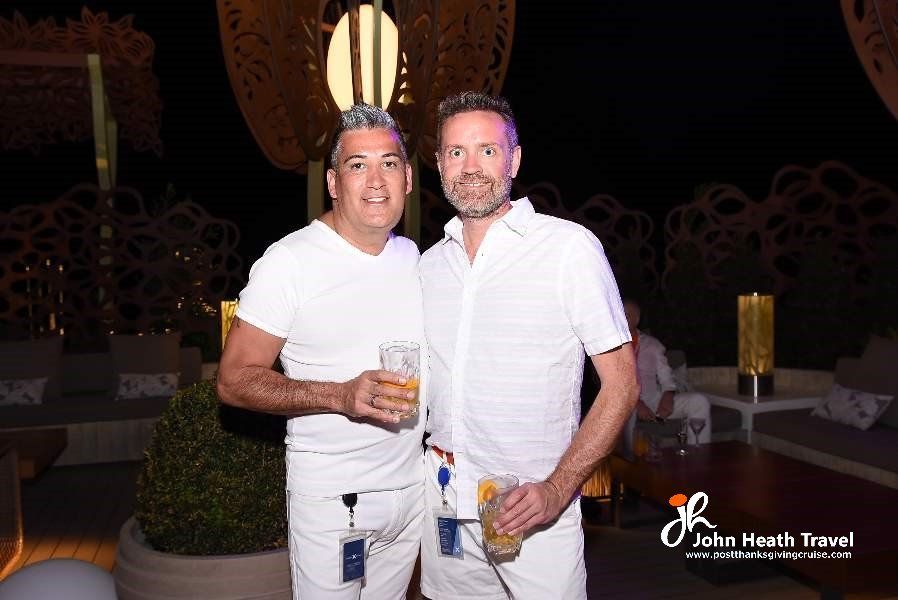 Two men in white shirts are standing next to each other holding drinks.