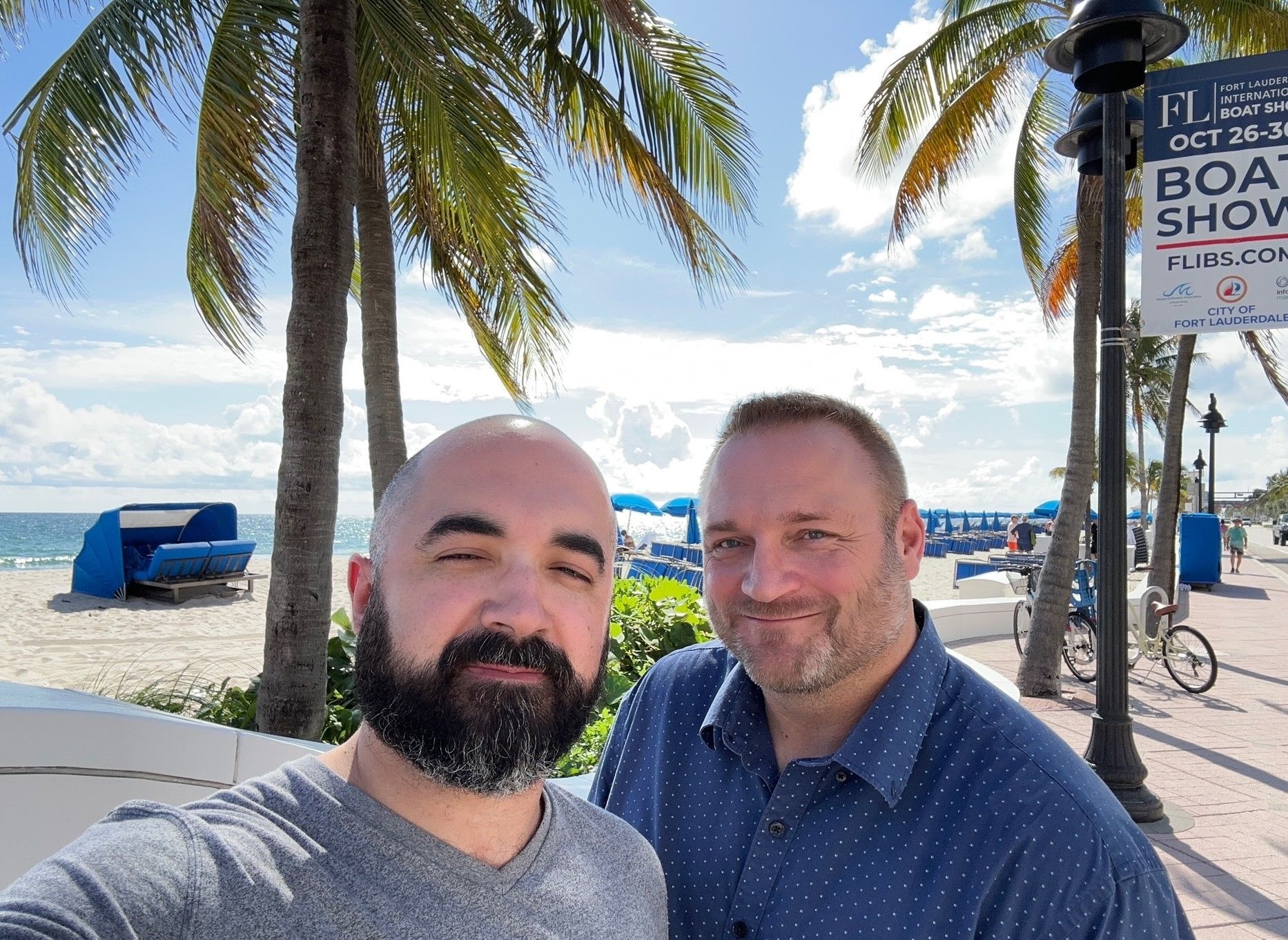 A man wearing glasses is smiling in front of a beach