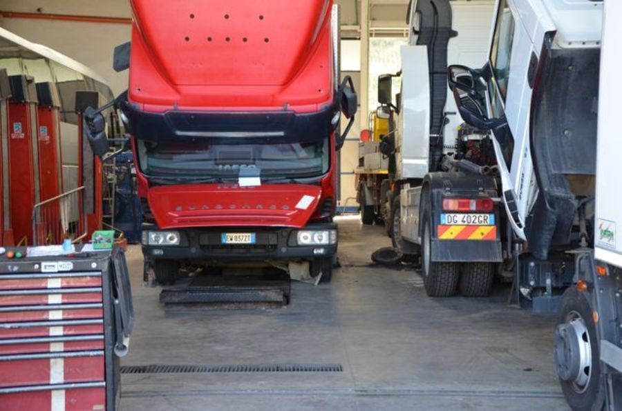 Camion rosso con cofano aperto all'interno di un garage; sono visibili altri camion e attrezzi.