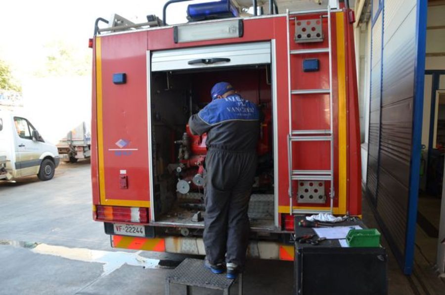 Una persona in uniforme blu e nera ripara il retro di un camion dei pompieri rosso.