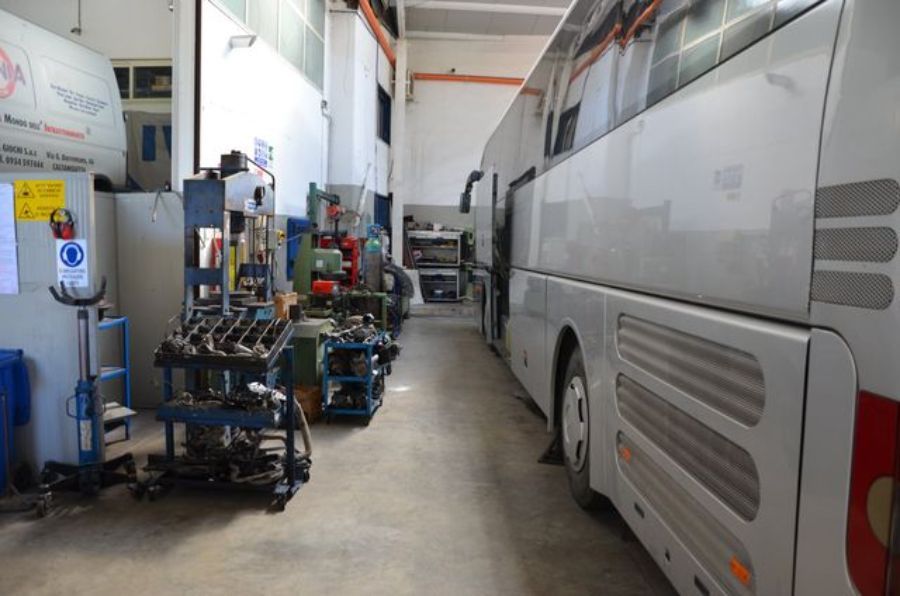 Autobus parcheggiato in un'officina con attrezzi e attrezzature visibili; autobus bianco e rosso.