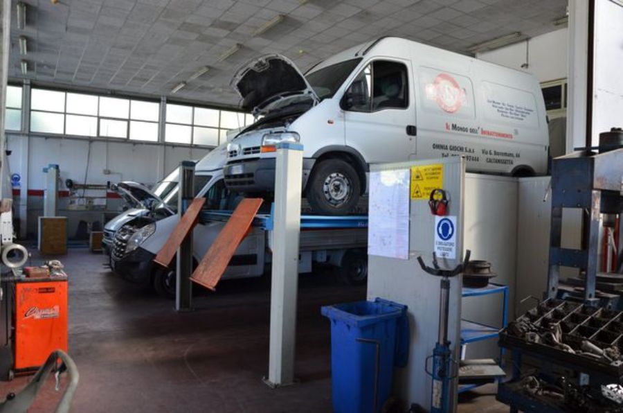 Officina di riparazione auto con veicoli sui ponti sollevatori, utensili e attrezzature visibili.