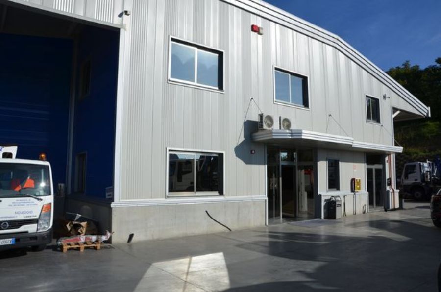 Un edificio industriale a due piani con banchina di carico e camion.