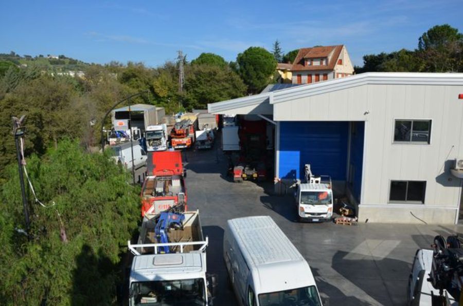 Camion parcheggiati presso un edificio commerciale con banchina di carico; giornata di sole.