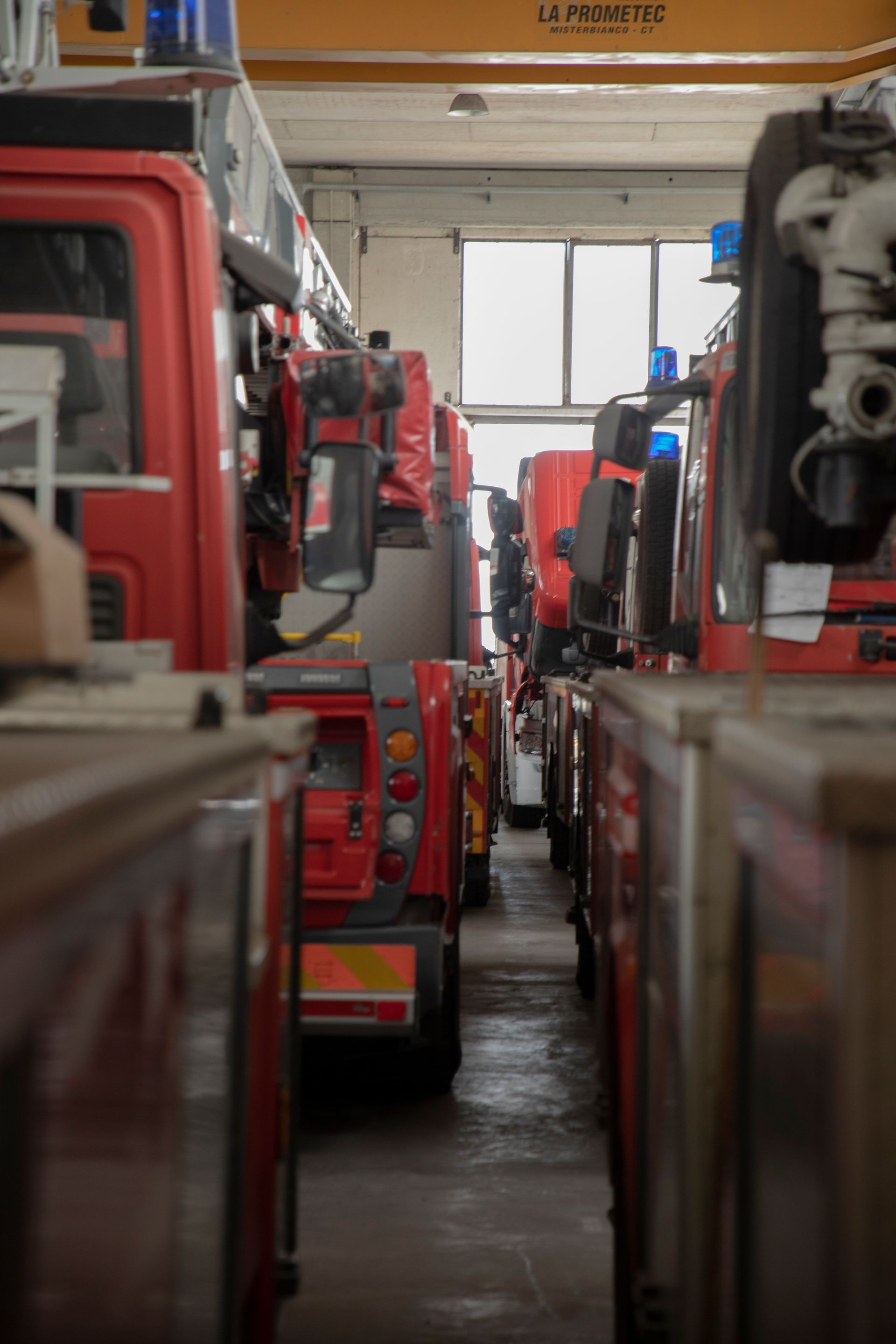 Camion dei pompieri allineati in un garage, rossi con luci blu, visti da una prospettiva dal basso.