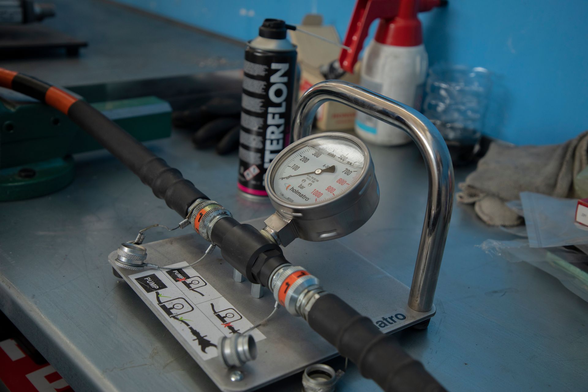 Un manometro collegato a un tubo nero, su un banco da lavoro in metallo. Sullo sfondo, una bomboletta spray e degli attrezzi.