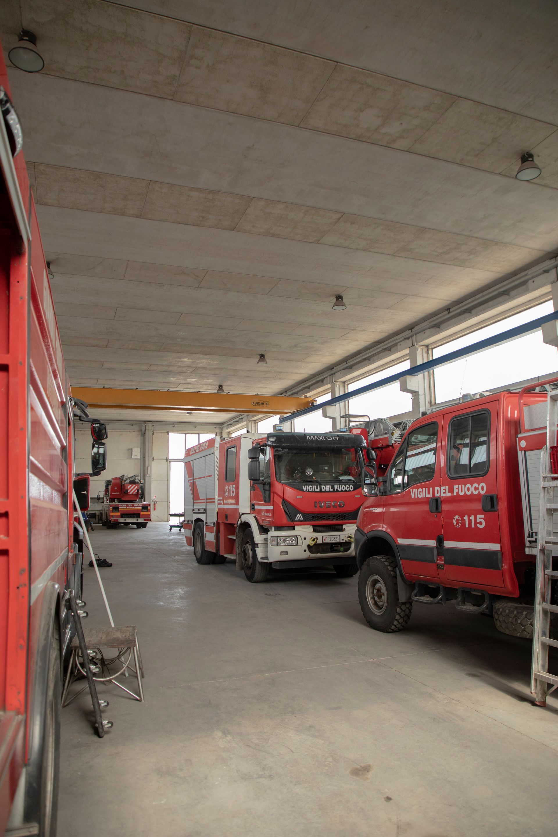 Camion dei pompieri parcheggiati all'interno di un garage; veicoli rossi e soffitto di cemento.