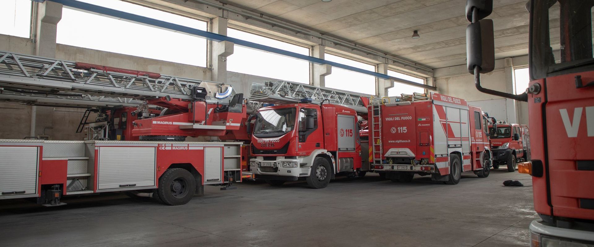 Camion dei pompieri parcheggiati all'interno di un garage. Veicoli rossi e bianchi con grandi scale, sotto un soffitto alto.