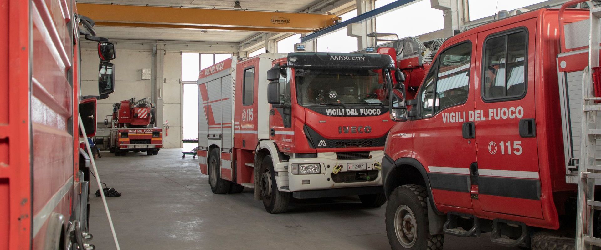 Camion dei pompieri parcheggiati all'interno di una caserma. I camion sono rossi. Sulla fiancata di uno di essi c'è la scritta