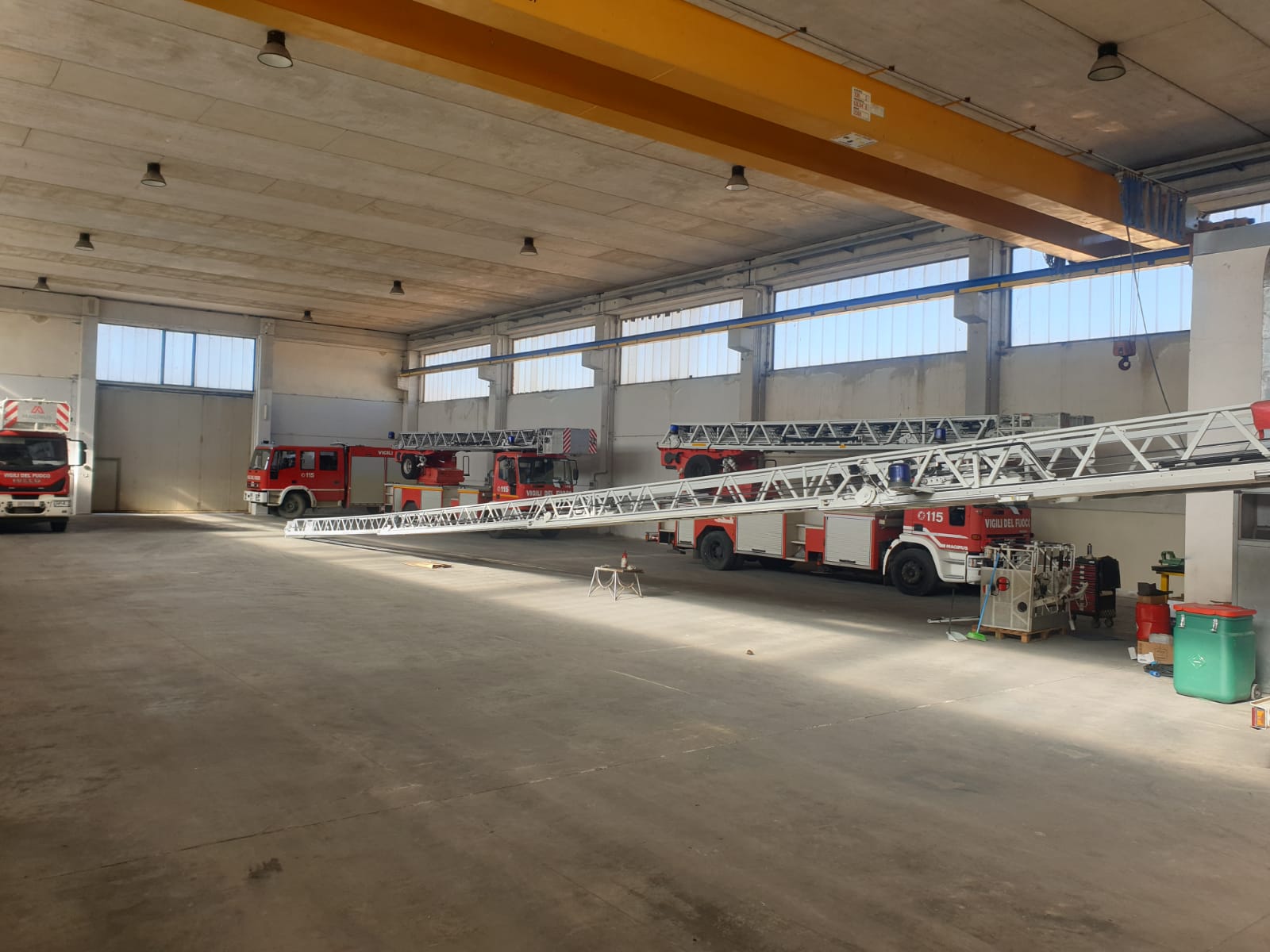Camion dei pompieri parcheggiati all'interno di un grande garage; uno di essi è dotato di una scala allungabile.