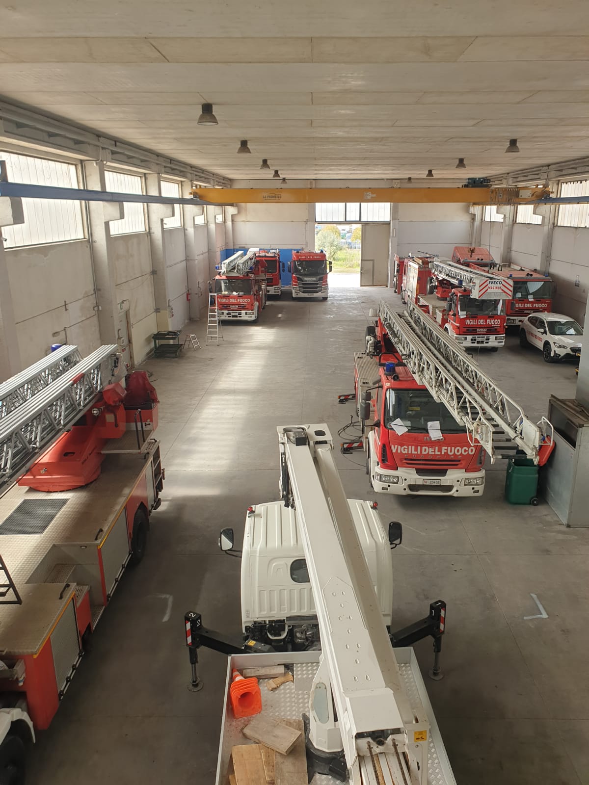 Camion dei pompieri all'interno di un garage; vista aerea. Diversi veicoli di emergenza rossi sono parcheggiati all'interno di un ampio piazzale aperto.