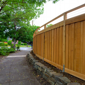 A picture of a wood privacy fence next to a sidewalk and trees.