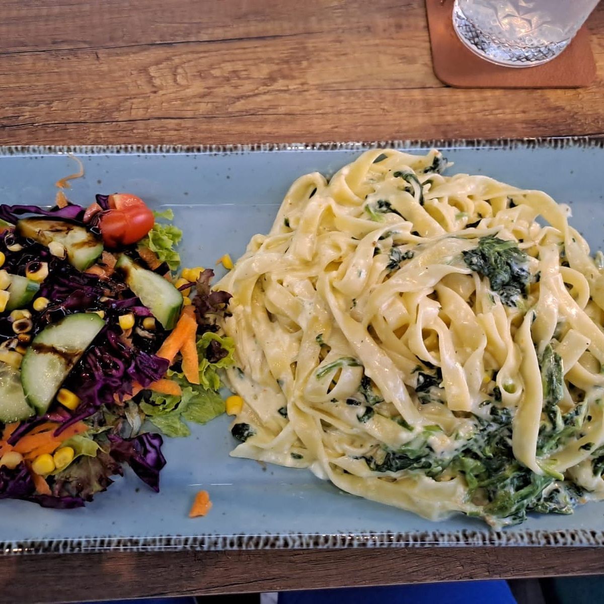 Nudeln mit Sahnesauce und Spinat, serviert auf einem blauen Teller mit einem Beilagensalat.