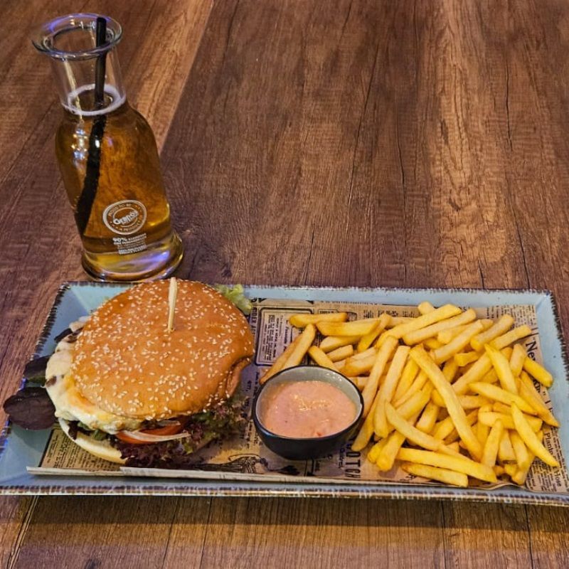 Burger mit Pommes und Bier auf einem Holztisch.