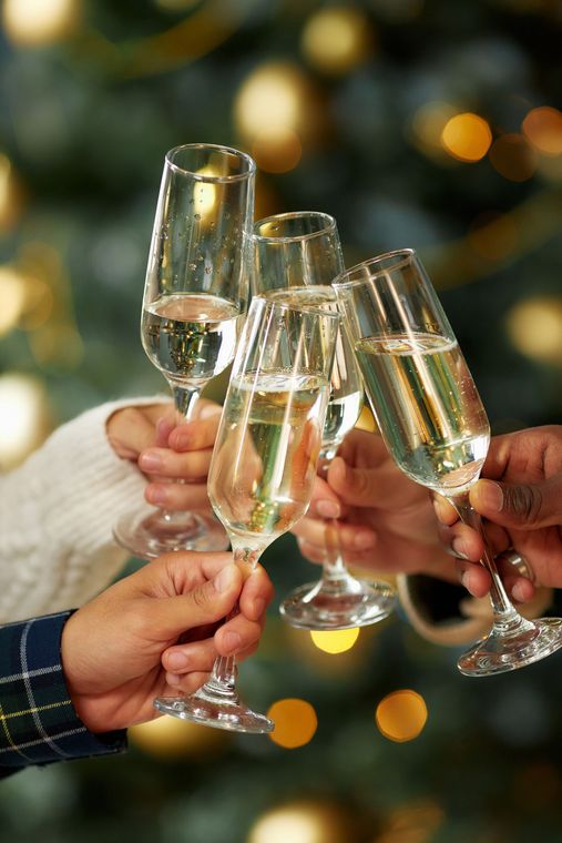 Menschen stoßen mit Champagnergläsern vor einem verschwommenen Weihnachtsbaum mit goldenen Lichtern an.