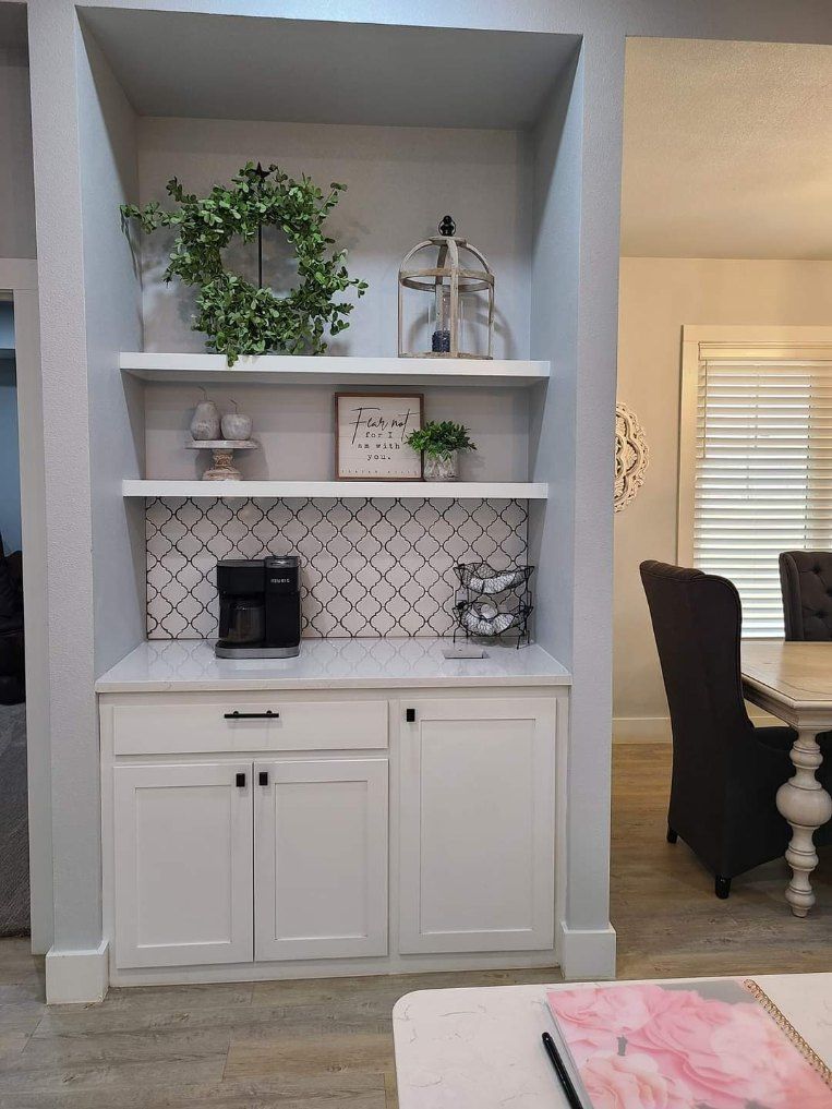 A kitchen with white cabinets , shelves , and a coffee maker.