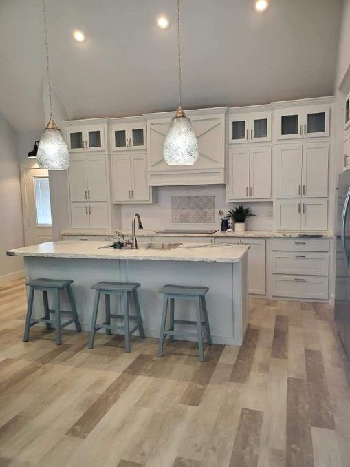 A kitchen with white cabinets , a large island , stools and a refrigerator.
