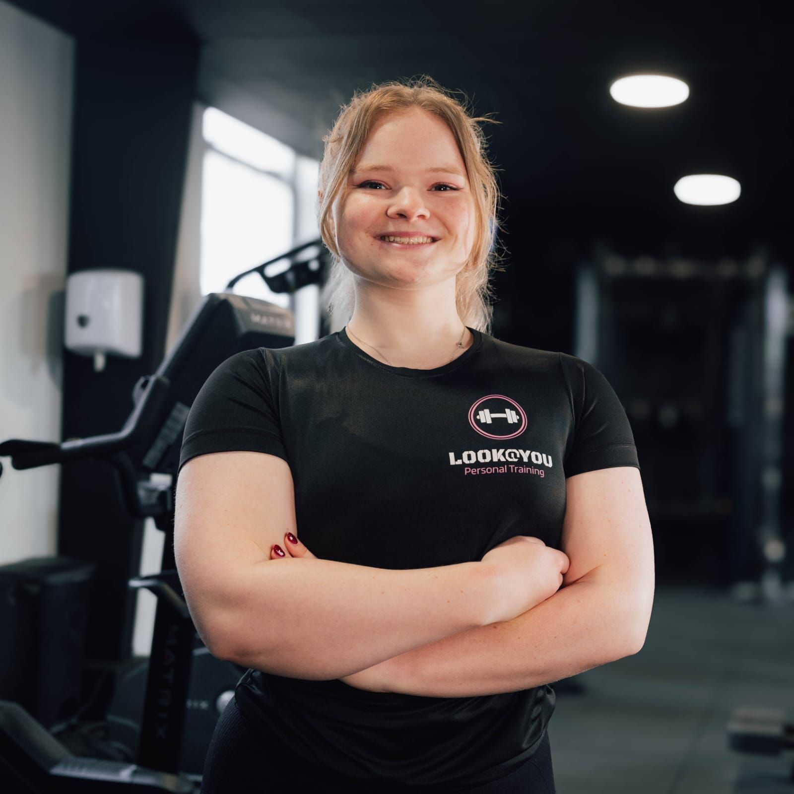 Een vrouw staat in een sportschool met haar armen over elkaar.