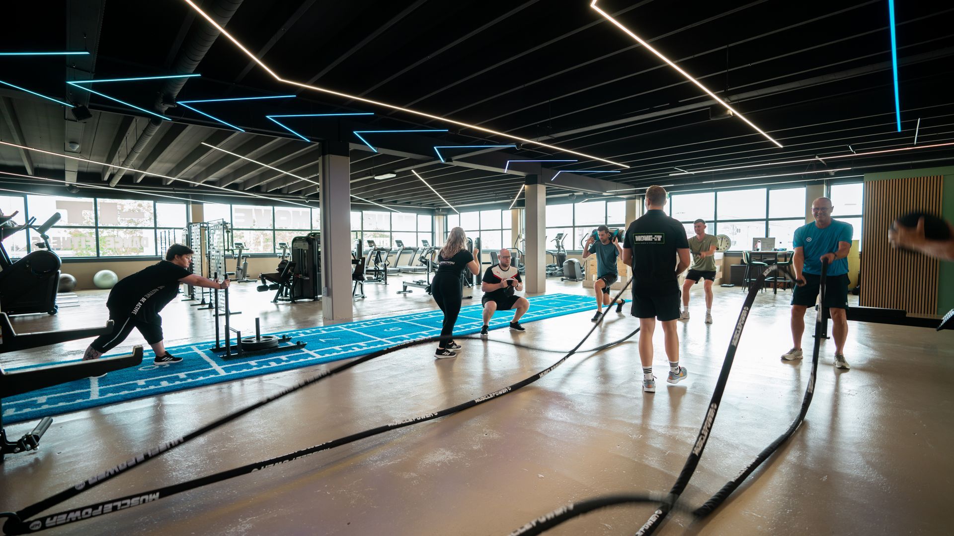 Een groep mensen doet squats op rode matten in een sportschool.