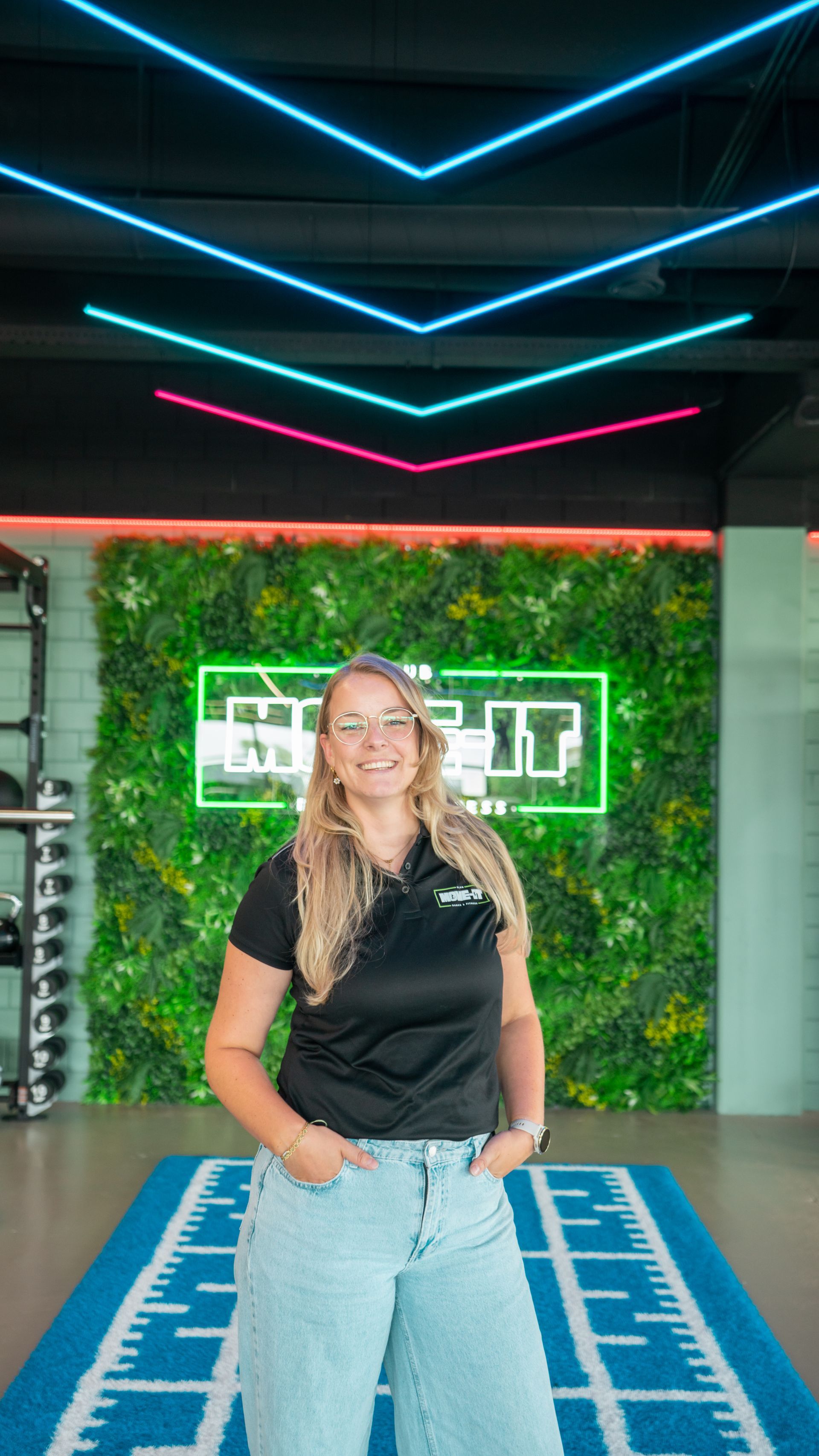 Een man in een zwart shirt staat met zijn armen over elkaar in een sportschool.