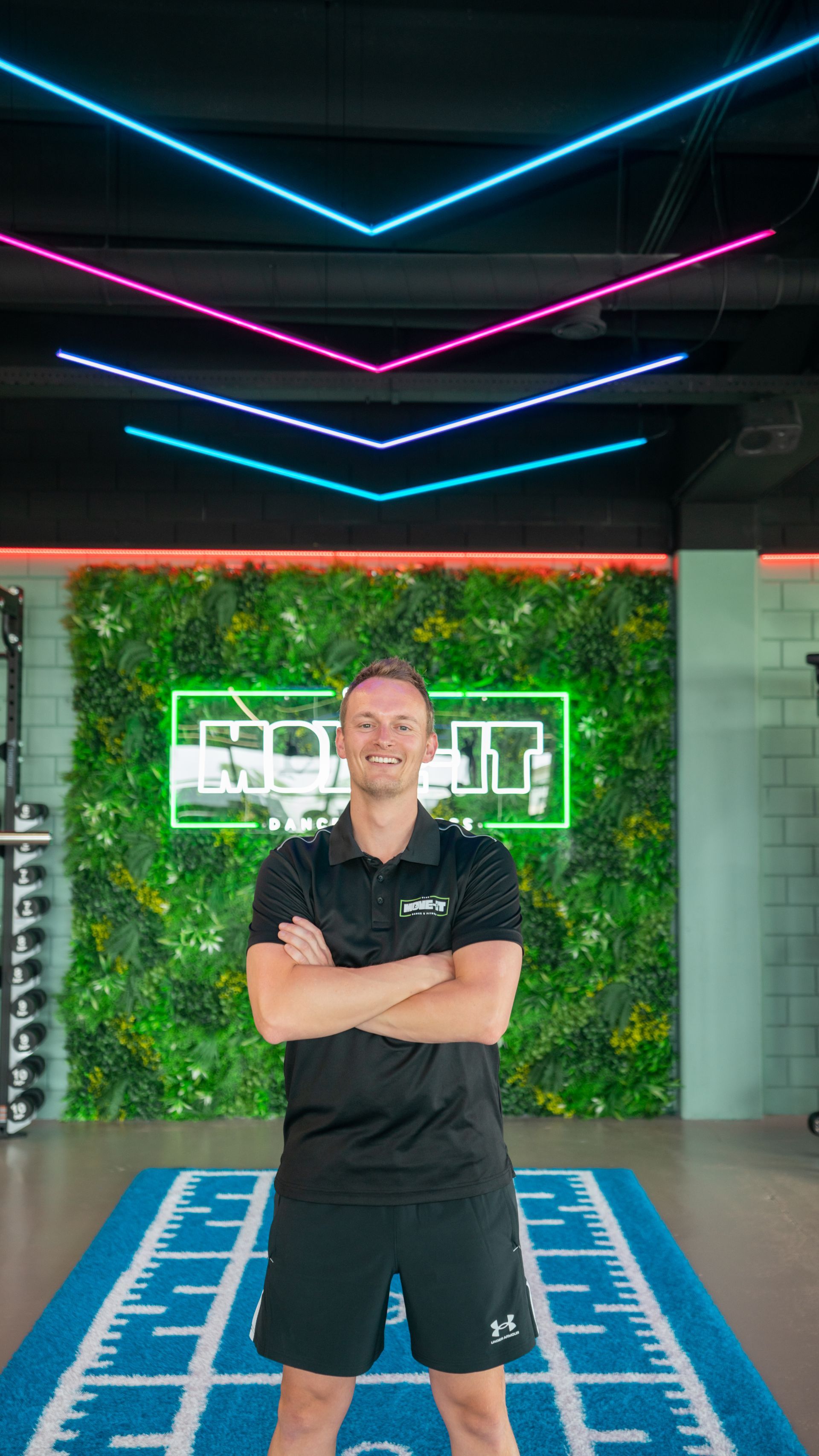 Een man in een zwart shirt staat met zijn armen over elkaar en lacht.