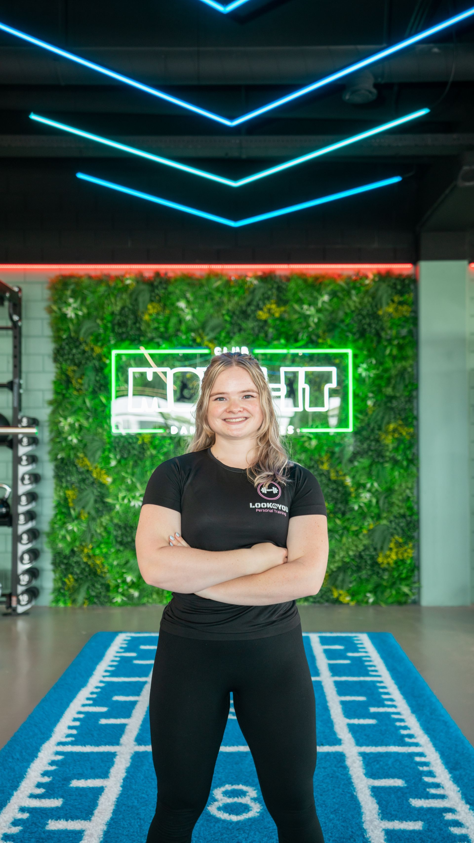 Een vrouw staat in een sportschool met haar armen over elkaar.