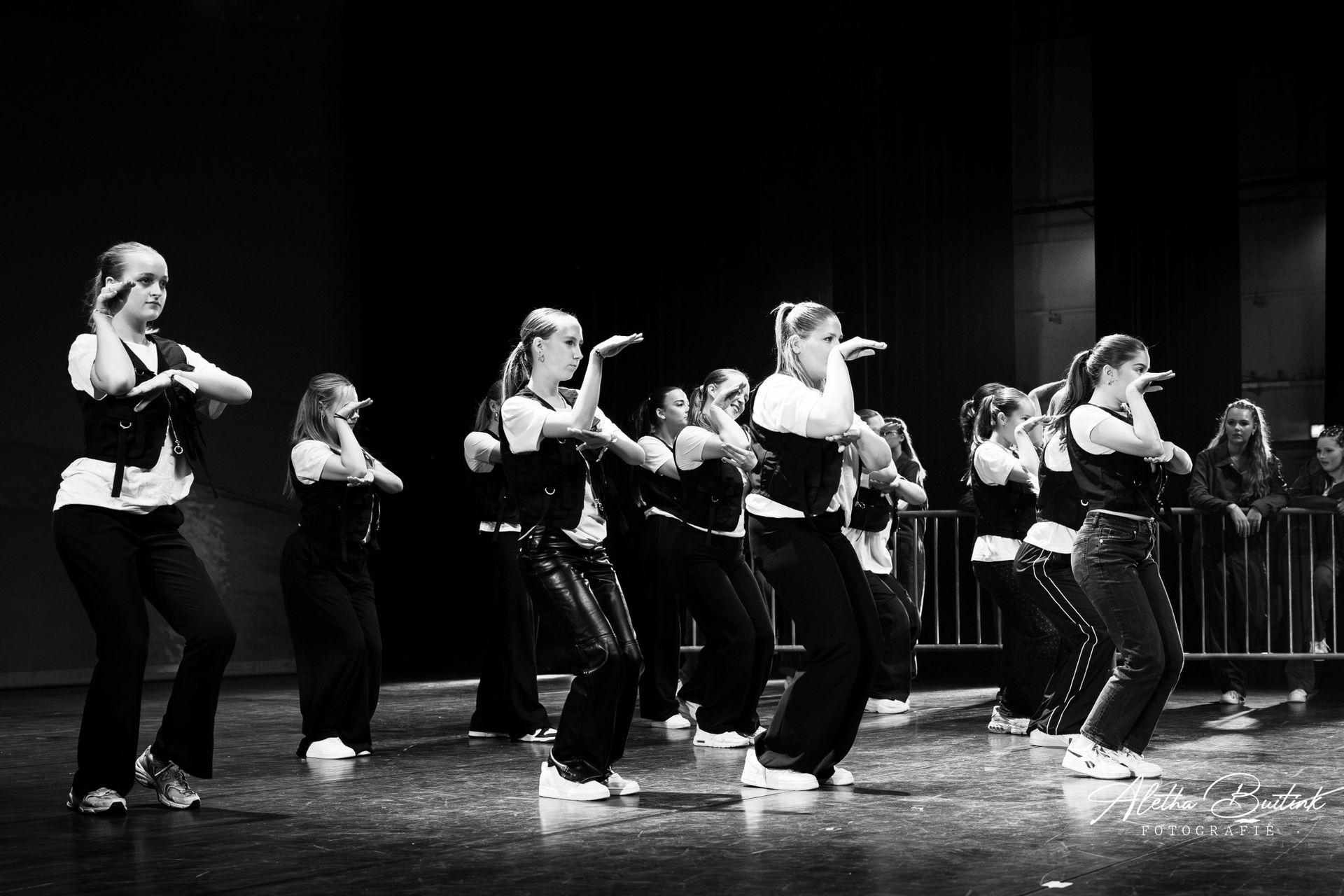 Op een zwart-witfoto is een groep jonge vrouwen te zien die op een podium danst.
