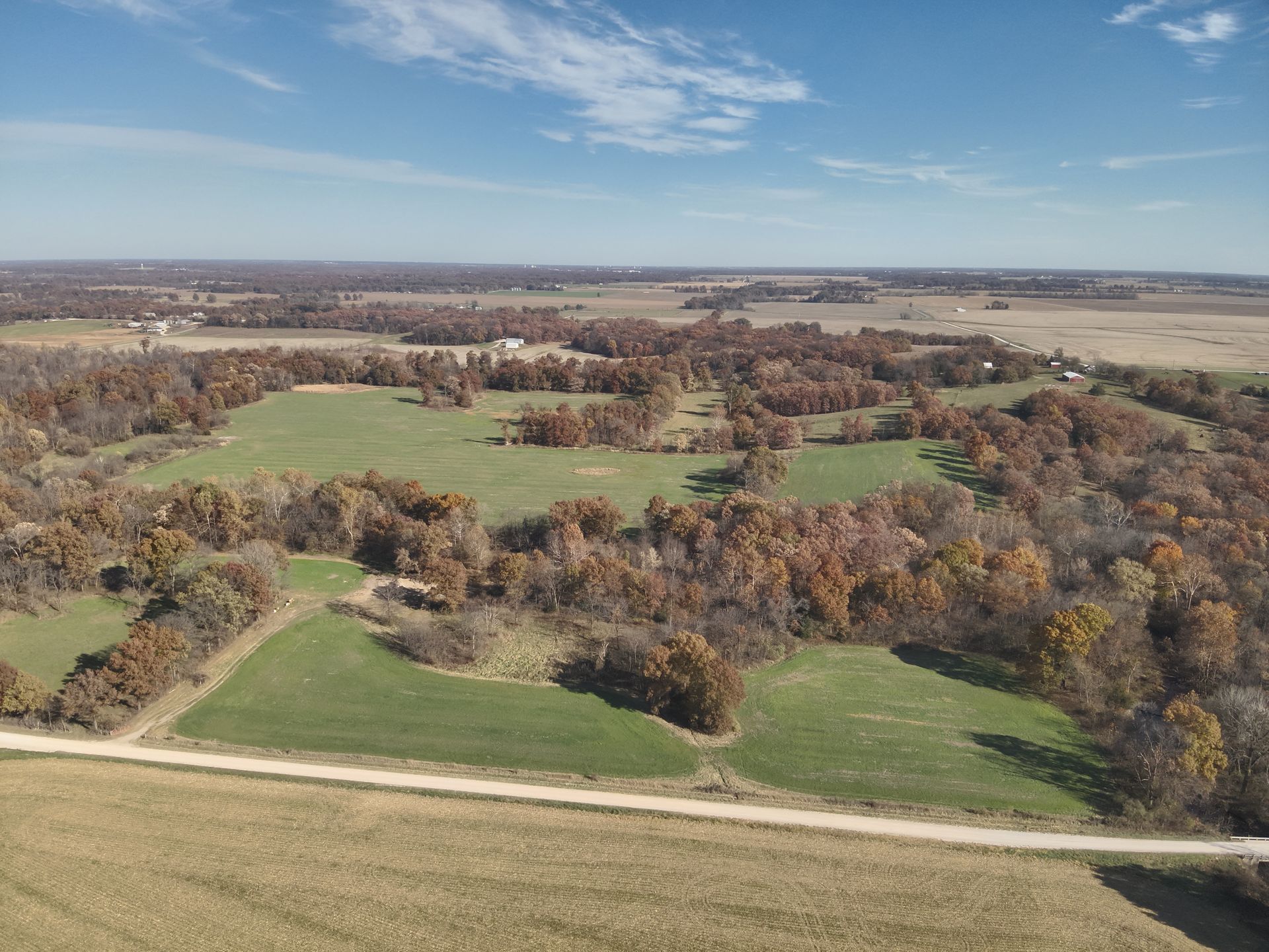 Aerial view of a rural landscape with fields, trees displaying fall colors, and a dirt road.