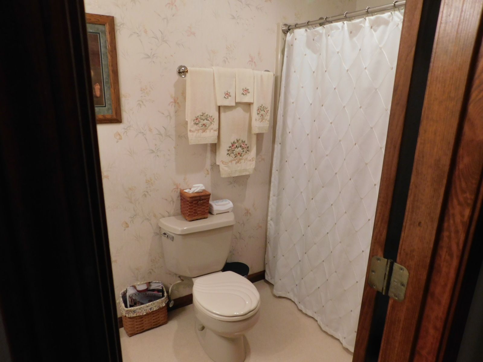A bathroom with a toilet , shower curtain , and towels hanging on the wall.