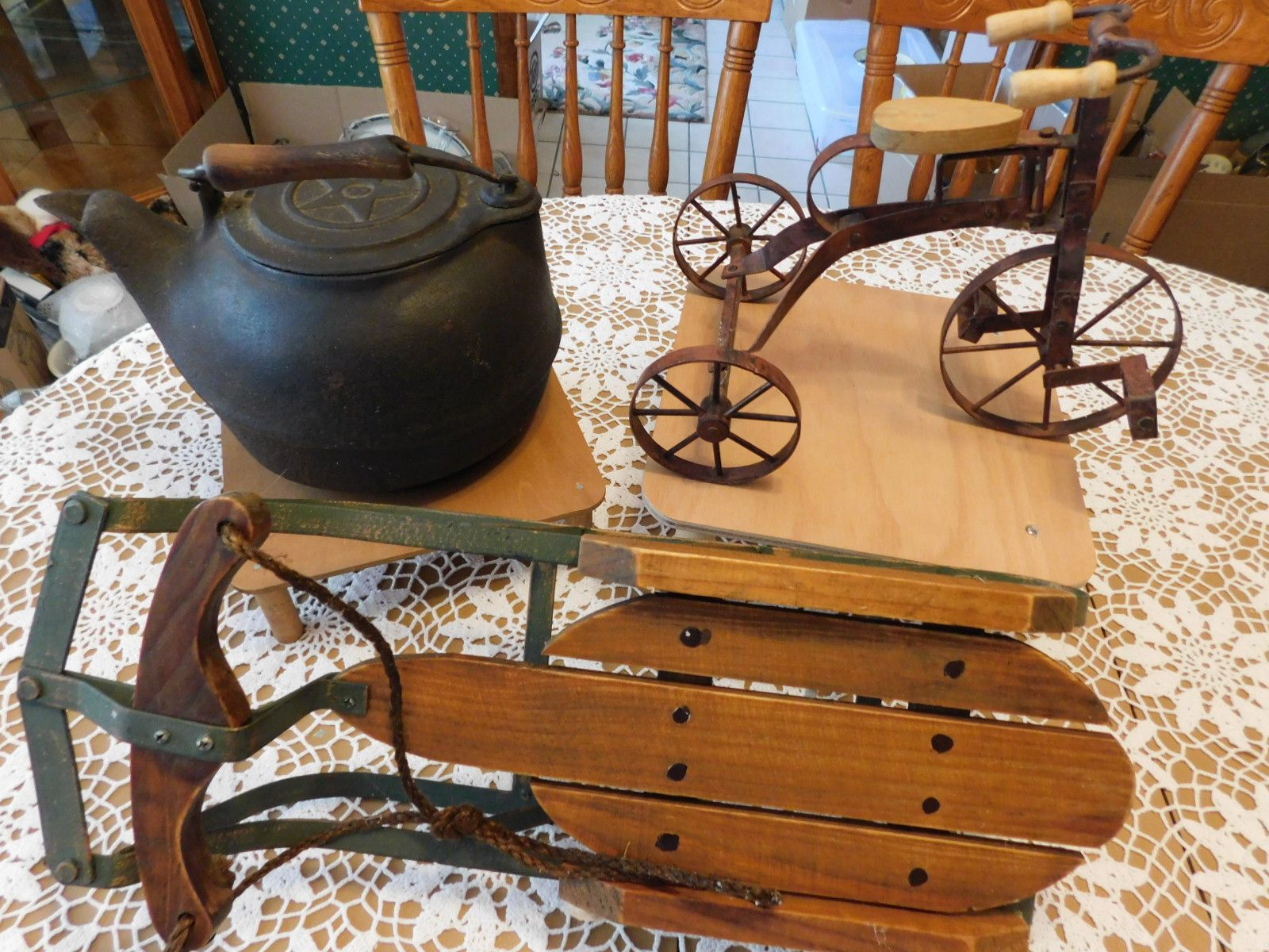 A tea kettle a tricycle and a sled are on a table