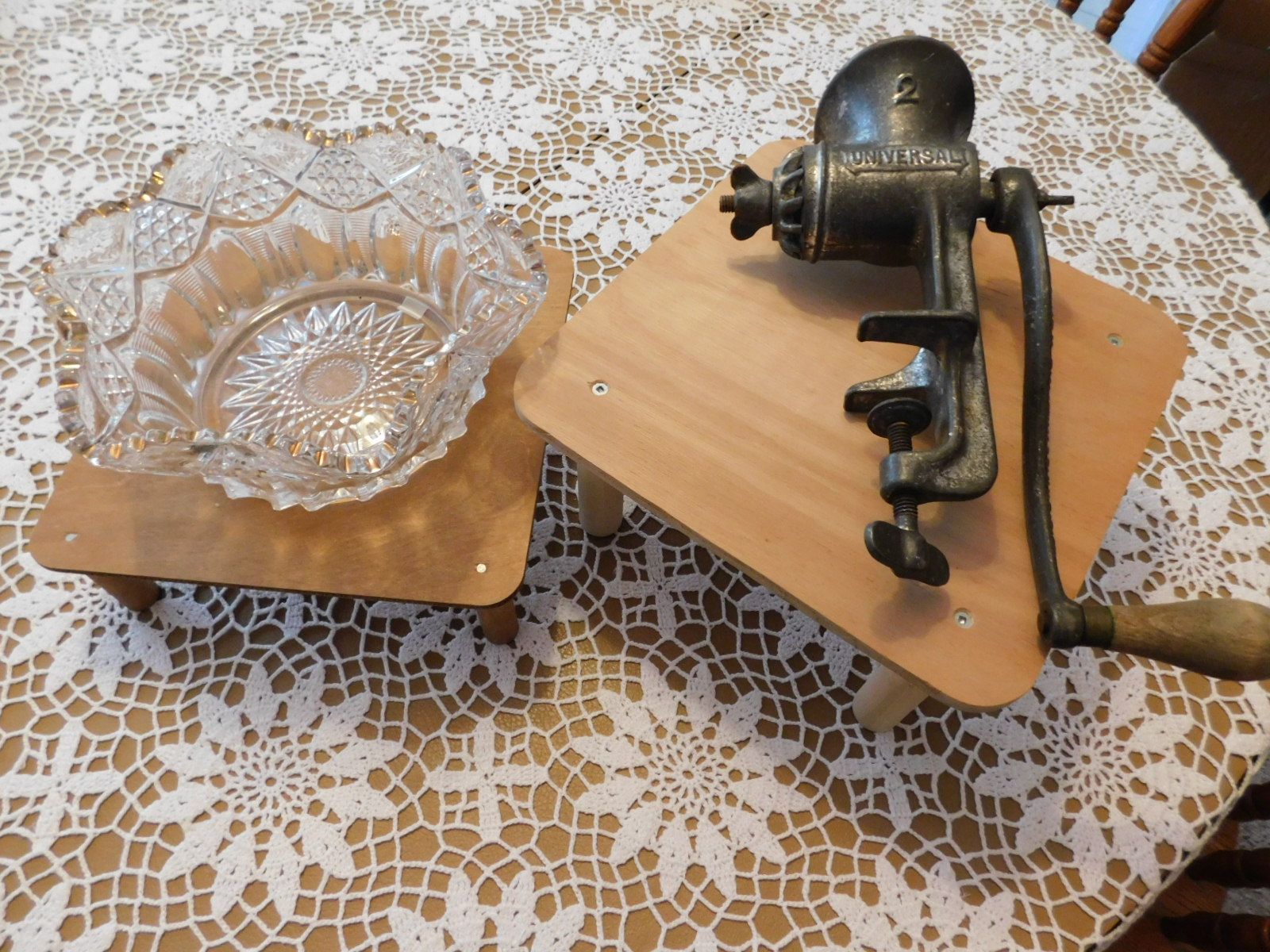 A meat grinder is sitting on a wooden table next to a glass bowl