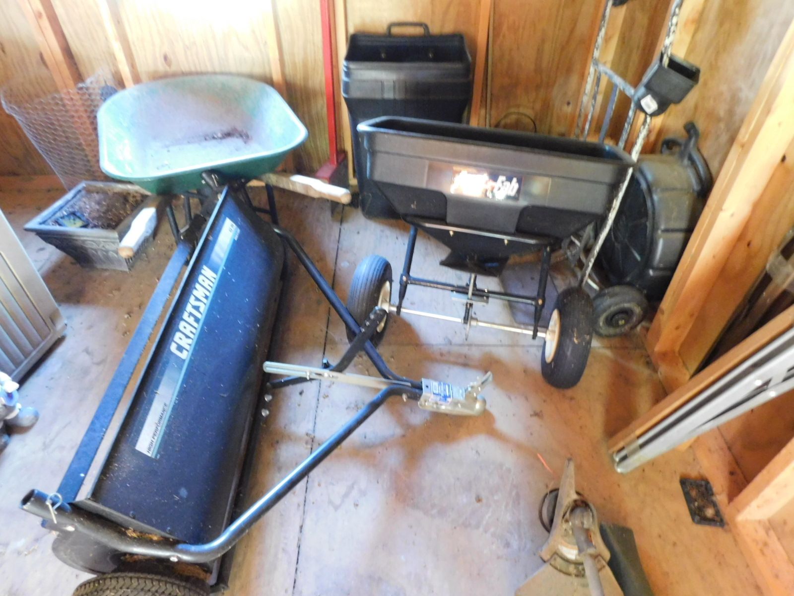 A wheelbarrow and a spreader are in a shed