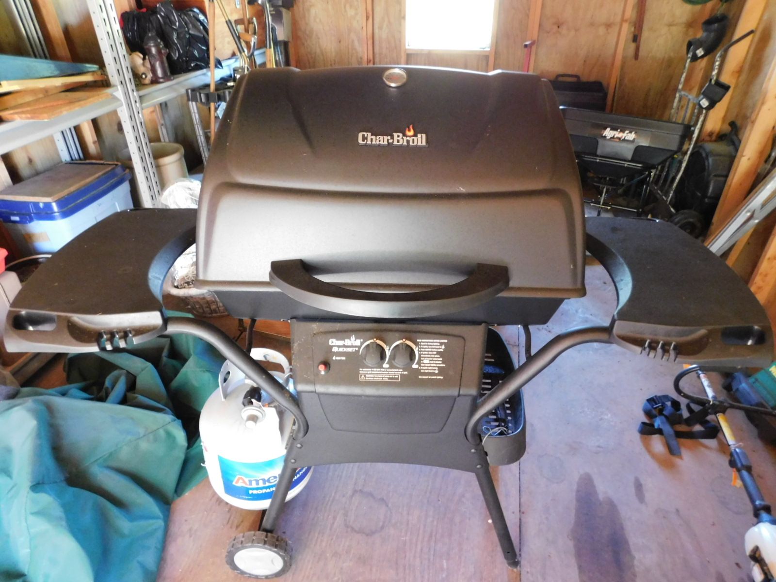 A black grill is sitting in a garage next to a propane tank