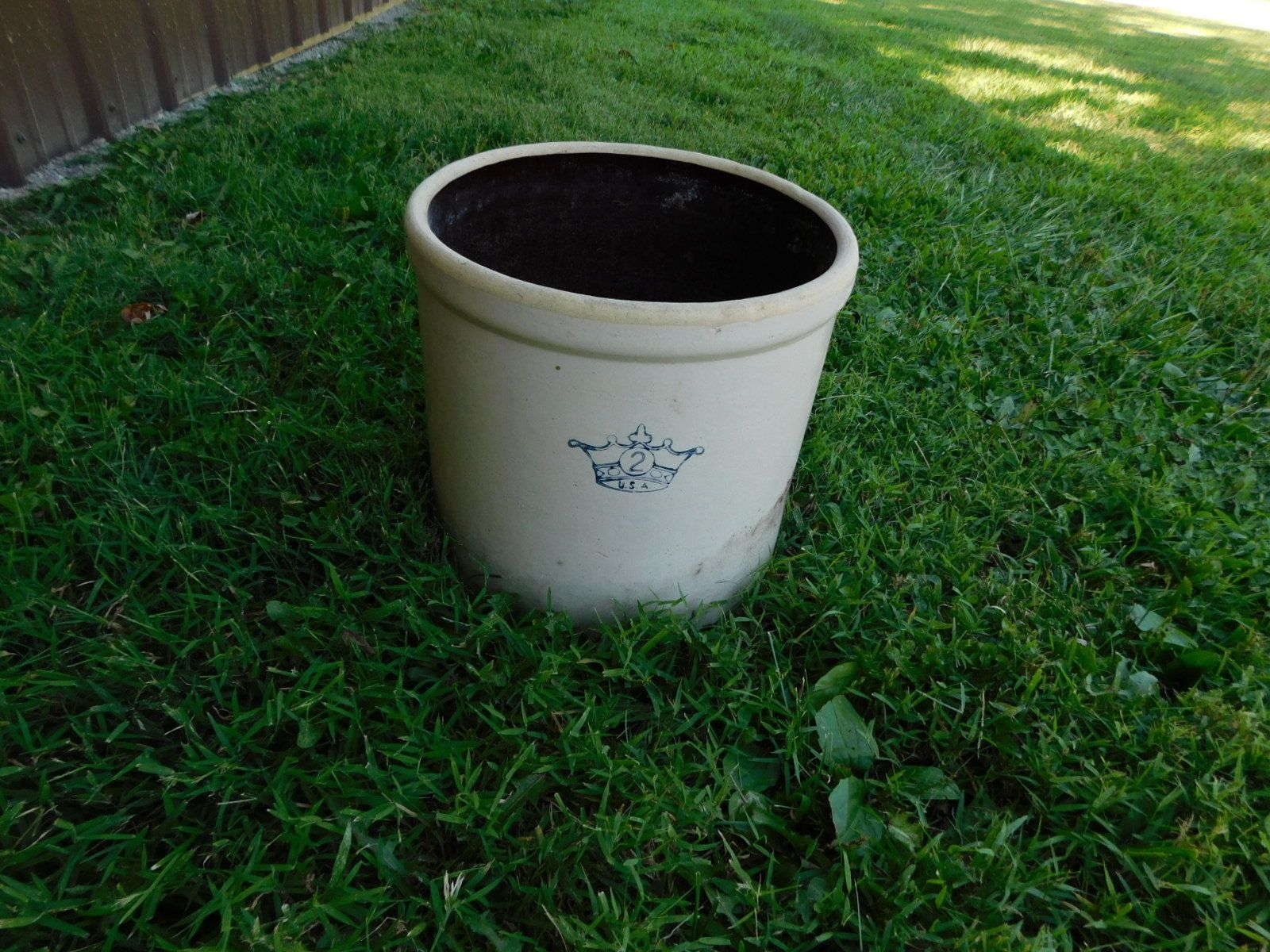 A white crock with a blue crown on it is sitting in the grass.