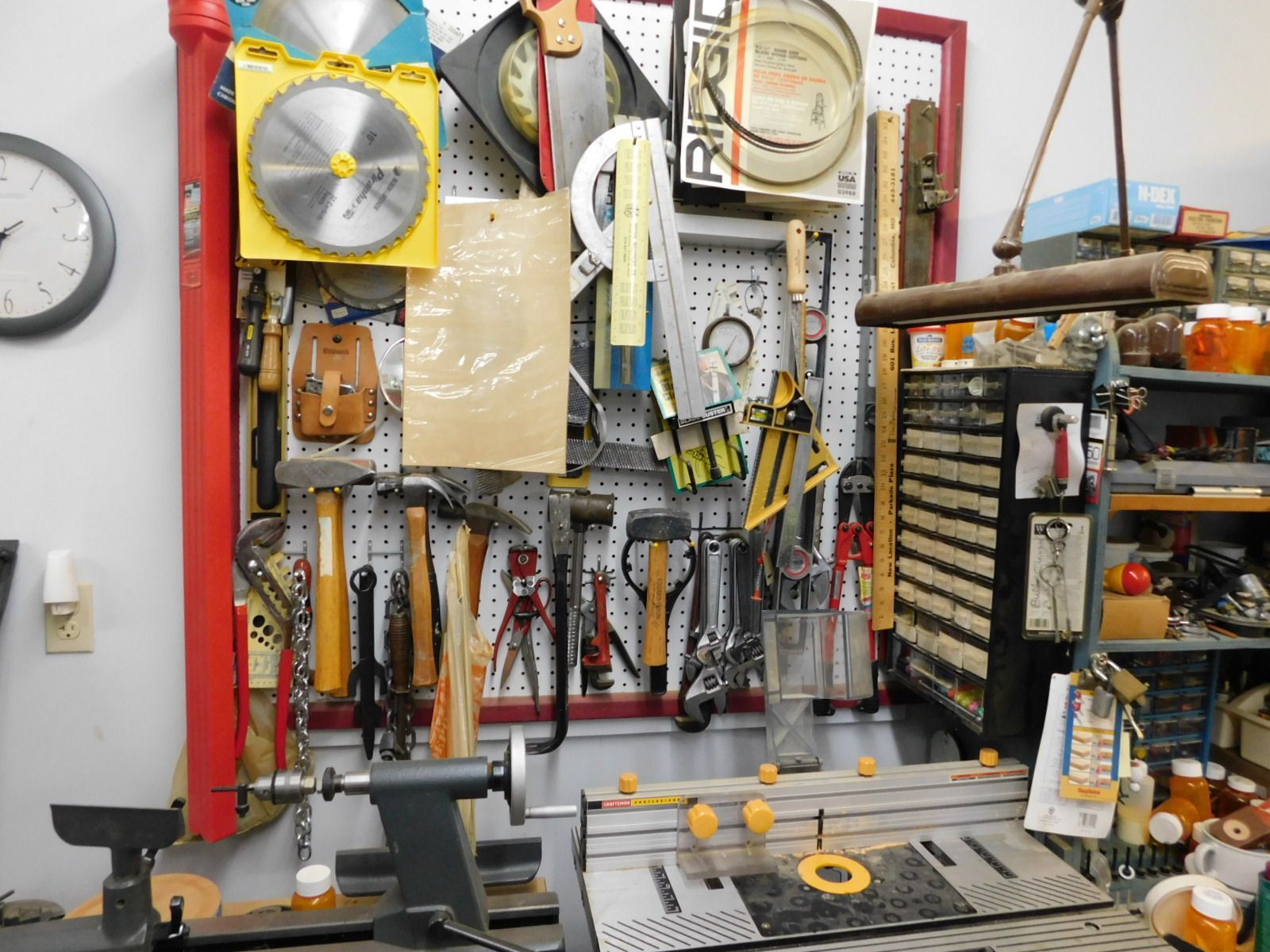 A clock hangs on a wall next to a shelf with tools and a sign that says rigid