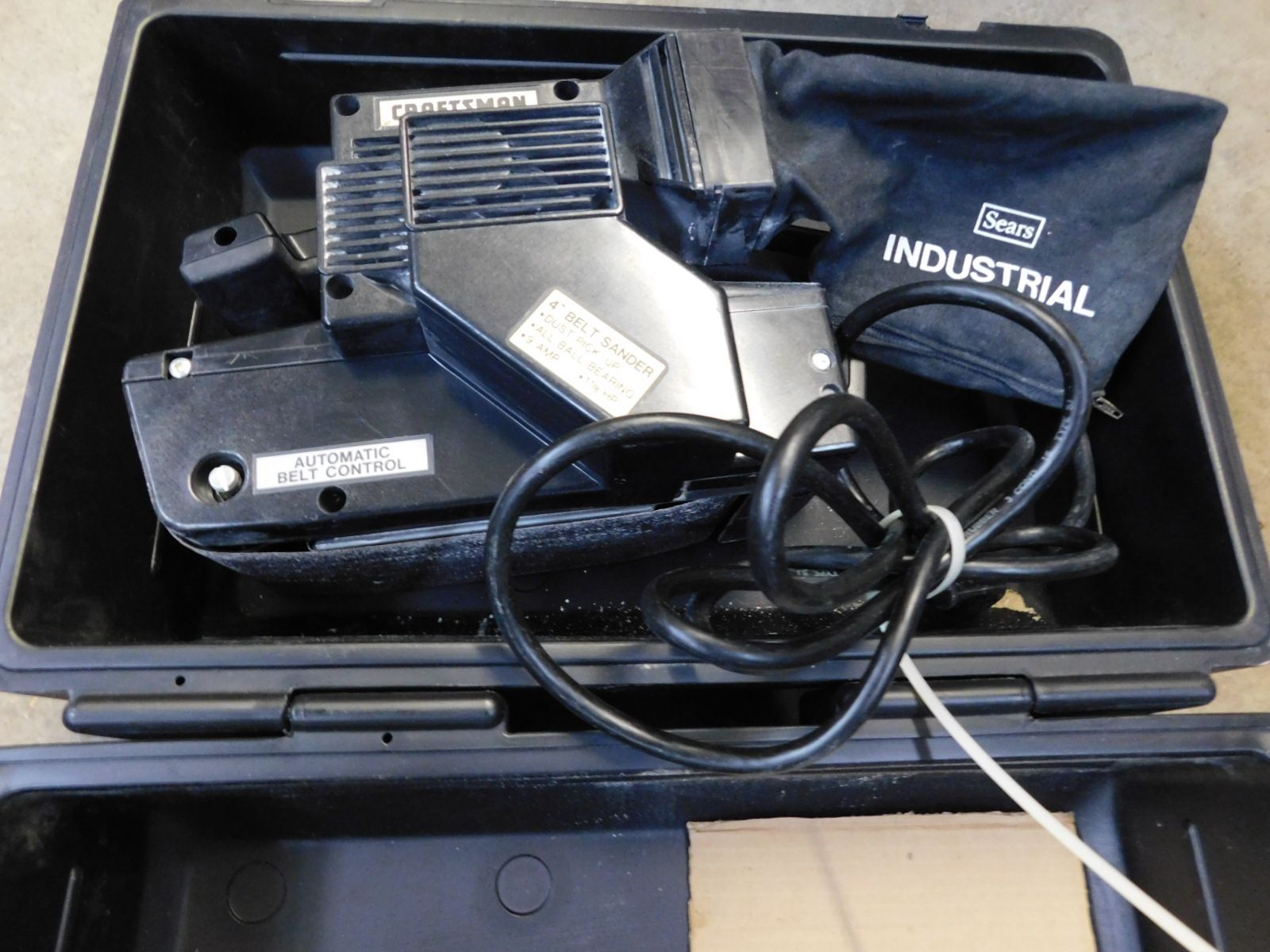 An industrial belt sander is in a black case