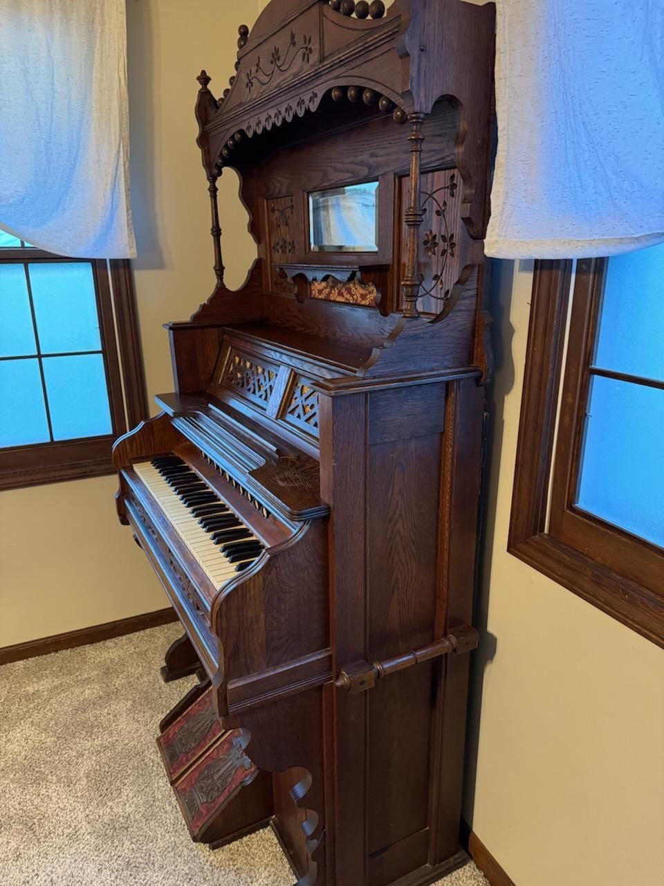 An antique organ is sitting in a room next to two windows.