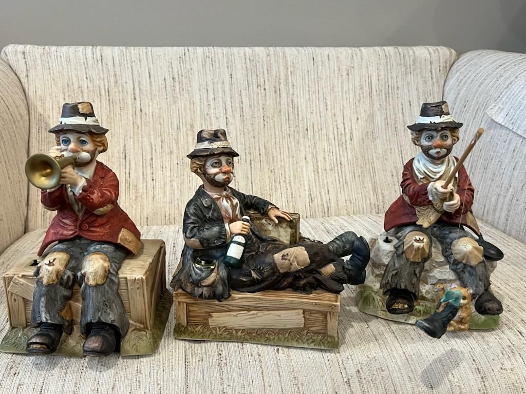 Three figurines of clowns are sitting on a couch.