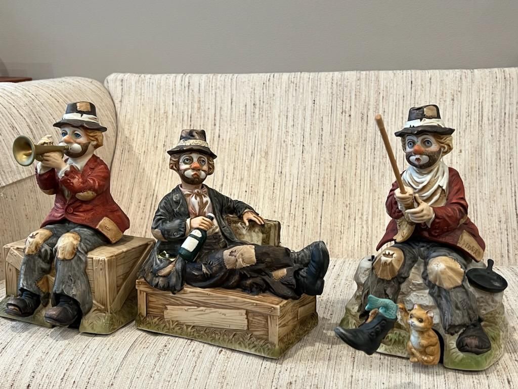 Three figurines of clowns are sitting on a couch.