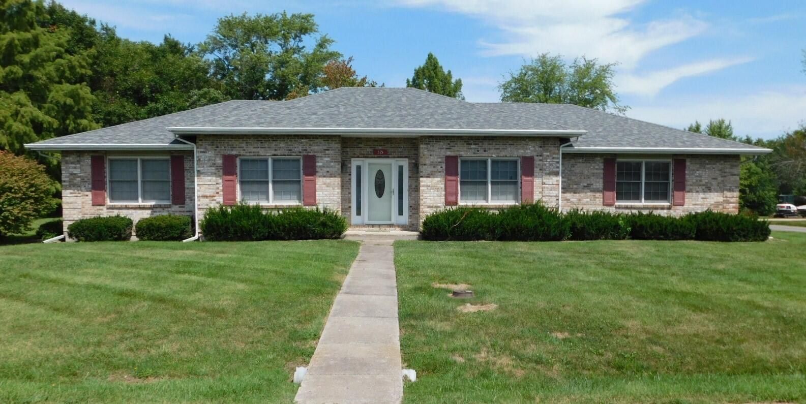 A brick ranch-style house with red shutters, a concrete walkway, and a well-manicured lawn.