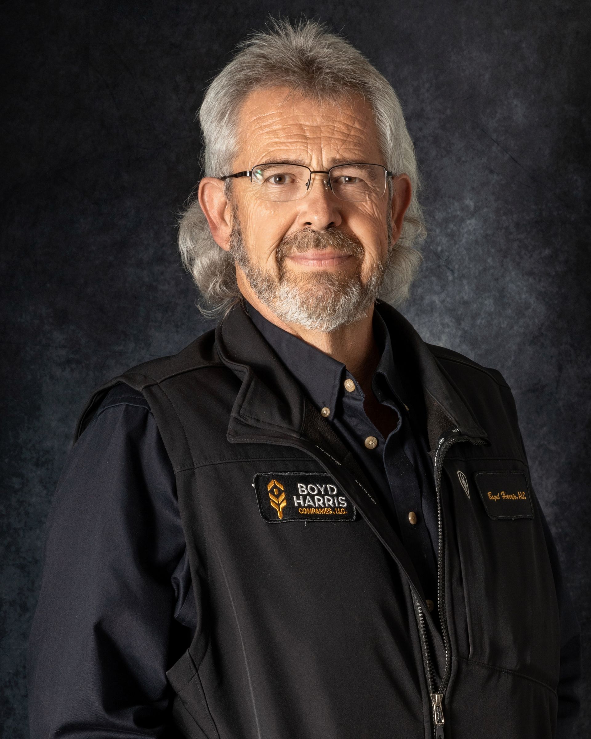 A man with a beard and glasses is wearing a vest and a white shirt.