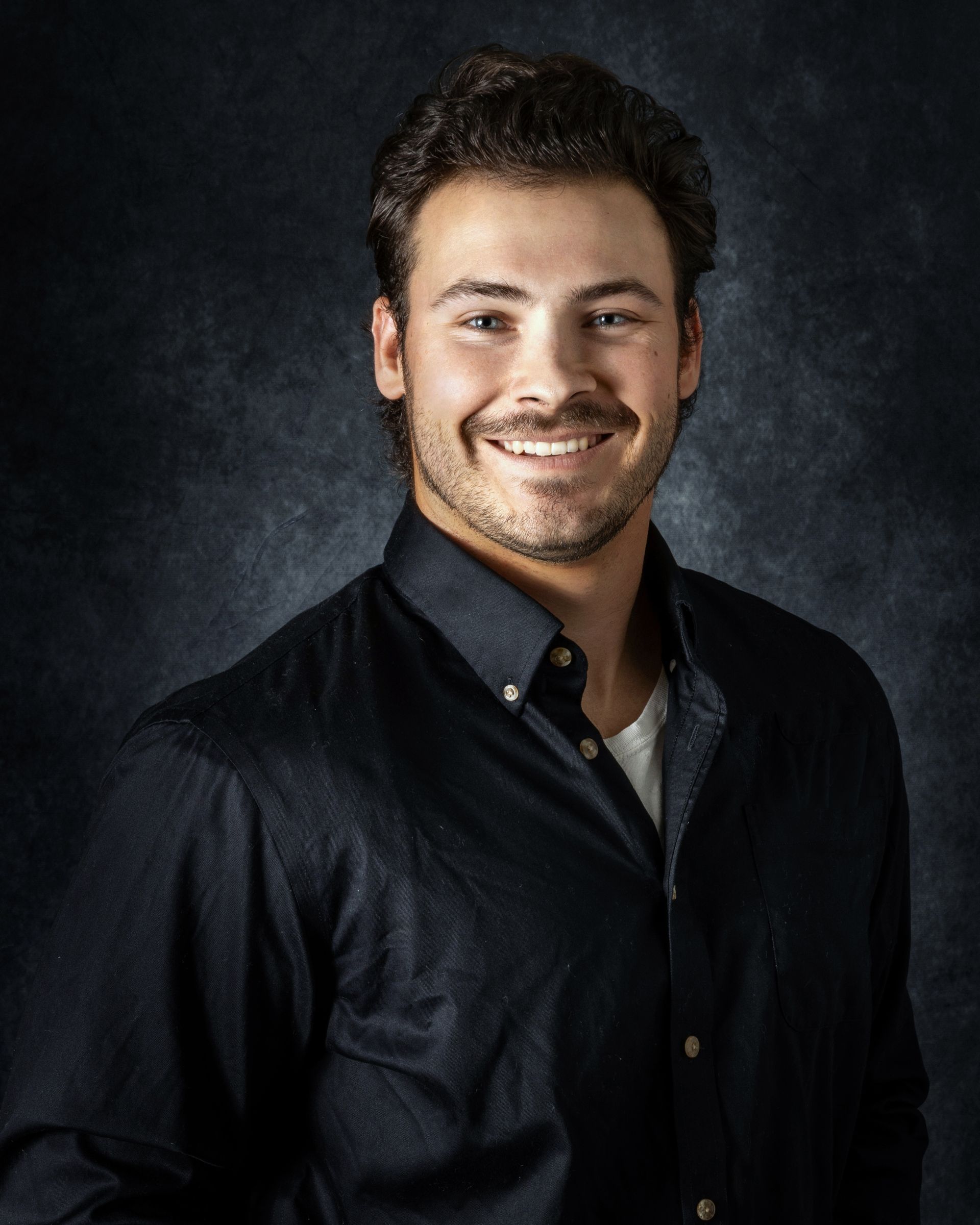 A young man wearing a white polo shirt smiles for the camera