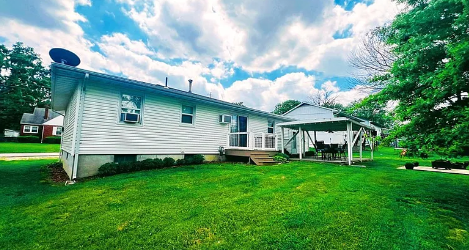 White house with green lawn, covered patio, and cloudy sky.