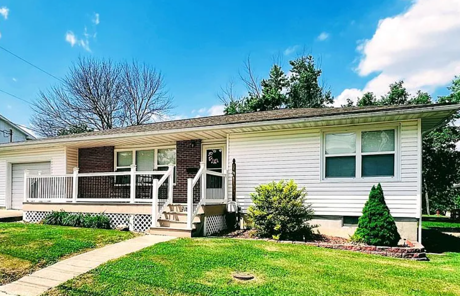 White ranch-style house with porch, brick accents, and green lawn under a blue sky.